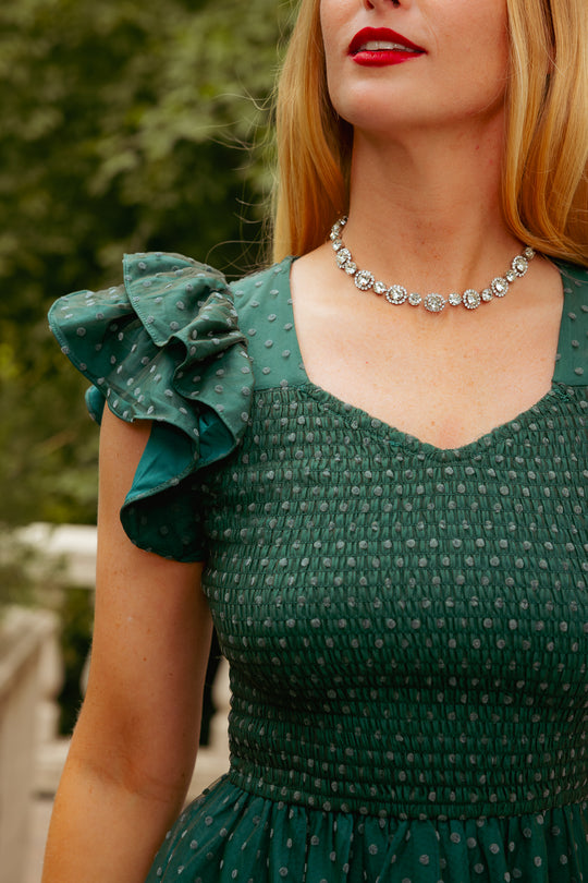 Woman wearing a green dress with ruffled sleeves and a silver necklace outdoors.