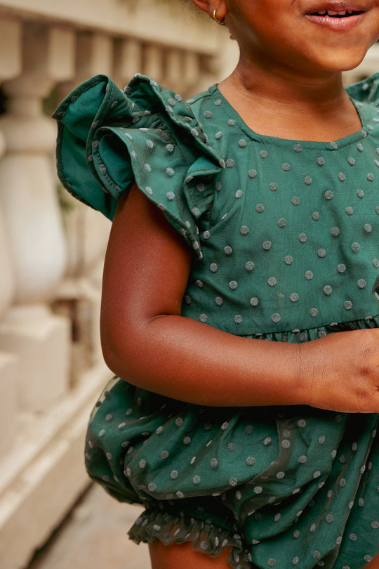 Child wearing a green polka dot dress with ruffled sleeves.