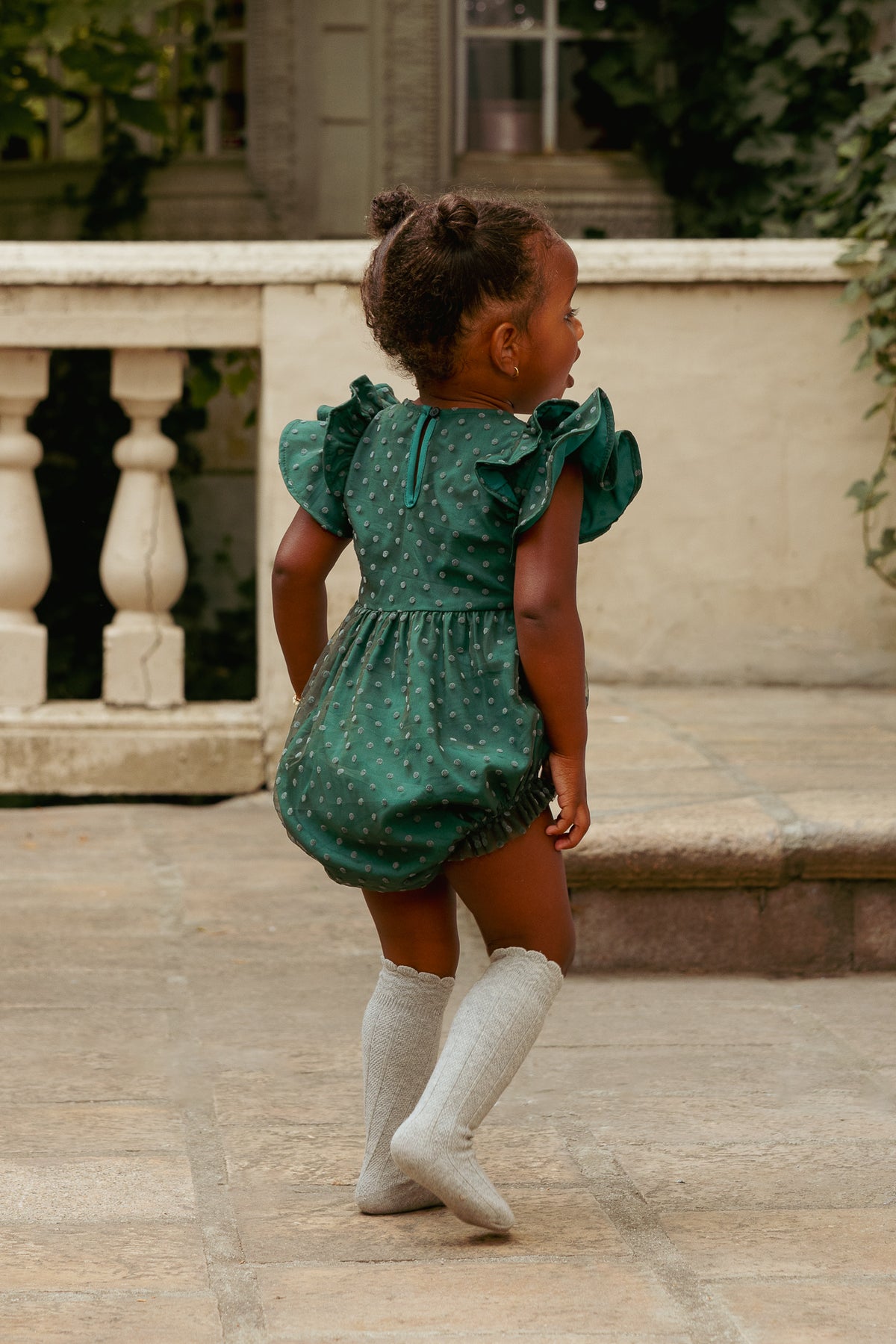 Child wearing a green polka dot romper with ruffled sleeves outdoors.