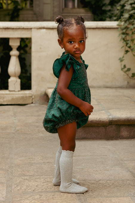 Young child wearing a green dress and white boots standing on a stone patio.