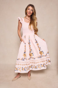 A woman models the Ivy City Co Hattie Dress in Embroidered Spring Floral, featuring ruffled cap sleeves and a maternity-friendly fit, styled with beige flats against a neutral background.