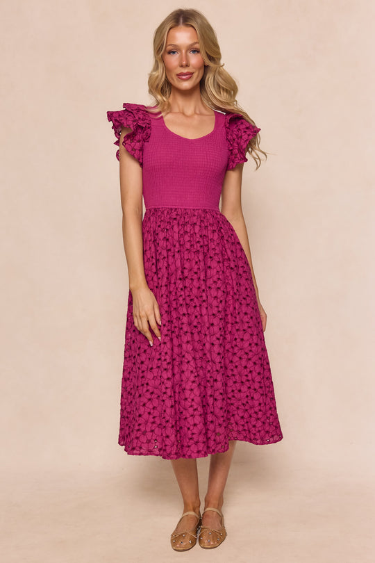 A woman with long blonde hair and beige sandals stands against a plain backdrop, wearing the Ivy City Co Hattie Dress in Magenta—a maternity-friendly piece with embroidery, ruffled sleeves, fitted bodice, and flowy patterned midi skirt.