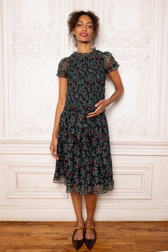 Woman wearing a patterned dress standing against a white wall.