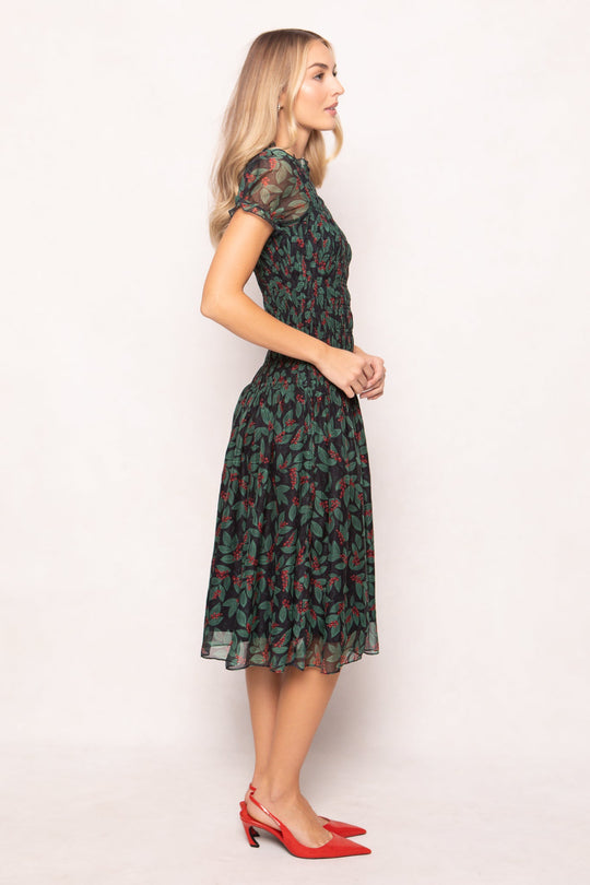 A woman wears a dark green, maternity-friendly Ivy City Co Hayden Dress in Berries featuring a berry and leaf print, paired with red slingback heels.