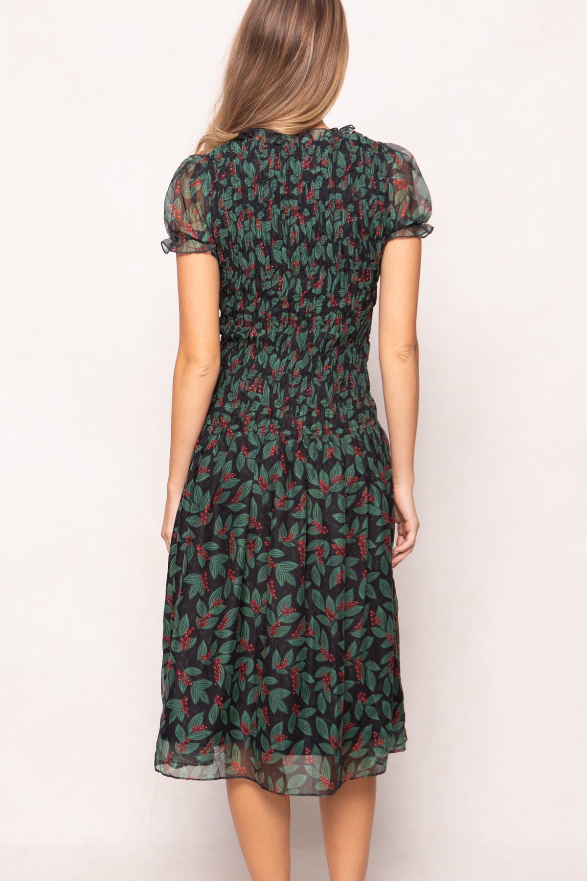 Back view of the Ivy City Co Hayden Dress in Berries featuring short puff sleeves, a smocked bodice, and a black skirt patterned with green leaves and red berries.