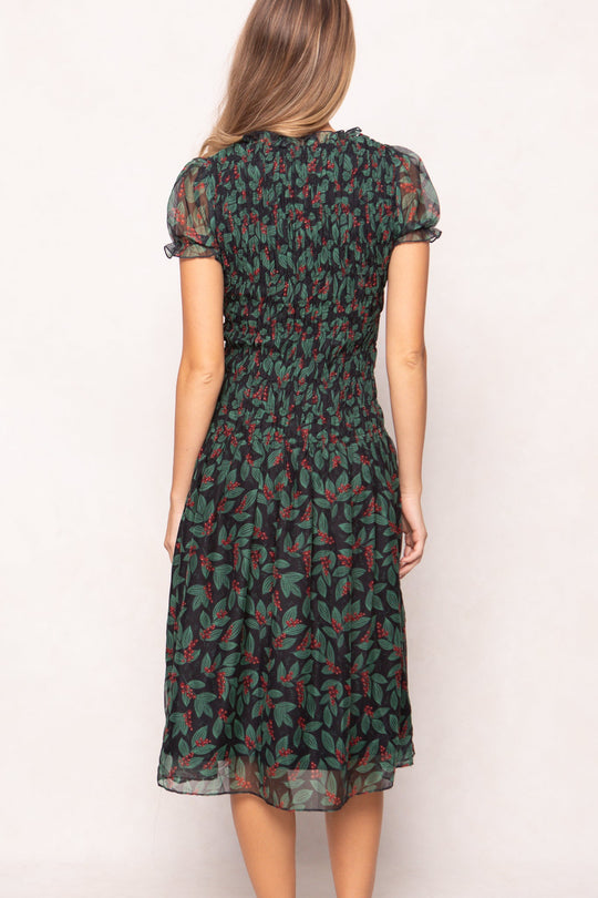 Back view of the Ivy City Co Hayden Dress in Berries featuring short puff sleeves, a smocked bodice, and a black skirt patterned with green leaves and red berries.