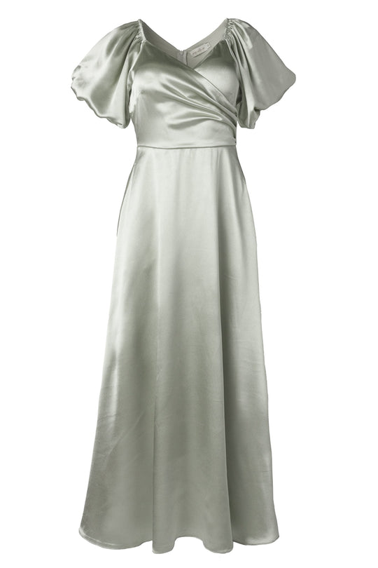 The Tessie Dress in Sage by Ivy City Co features a light green satin fabric with short puff sleeves, a V-neckline, and a fitted waist. Its wrap-style bodice and flowing, ankle-length skirt create an elegant bridesmaid dress that is both timeless and flattering.