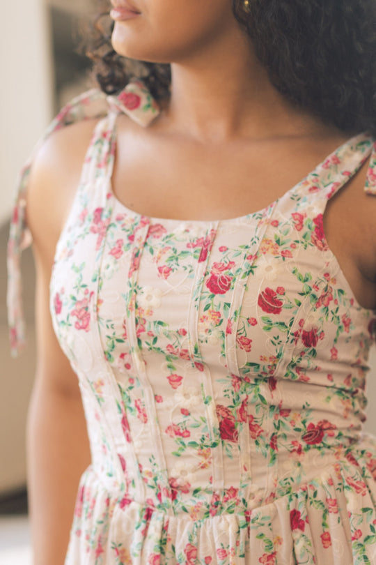 A person wearing the Ivy City Co Helene Dress in Vibrant Chintz, a sleeveless style with tied shoulder straps and a pink and green floral print. The photo highlights the upper body, with the full face not visible.