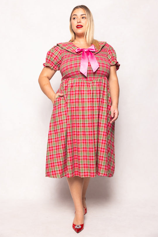 Woman wearing a red and green plaid dress with a pink bow on a white background