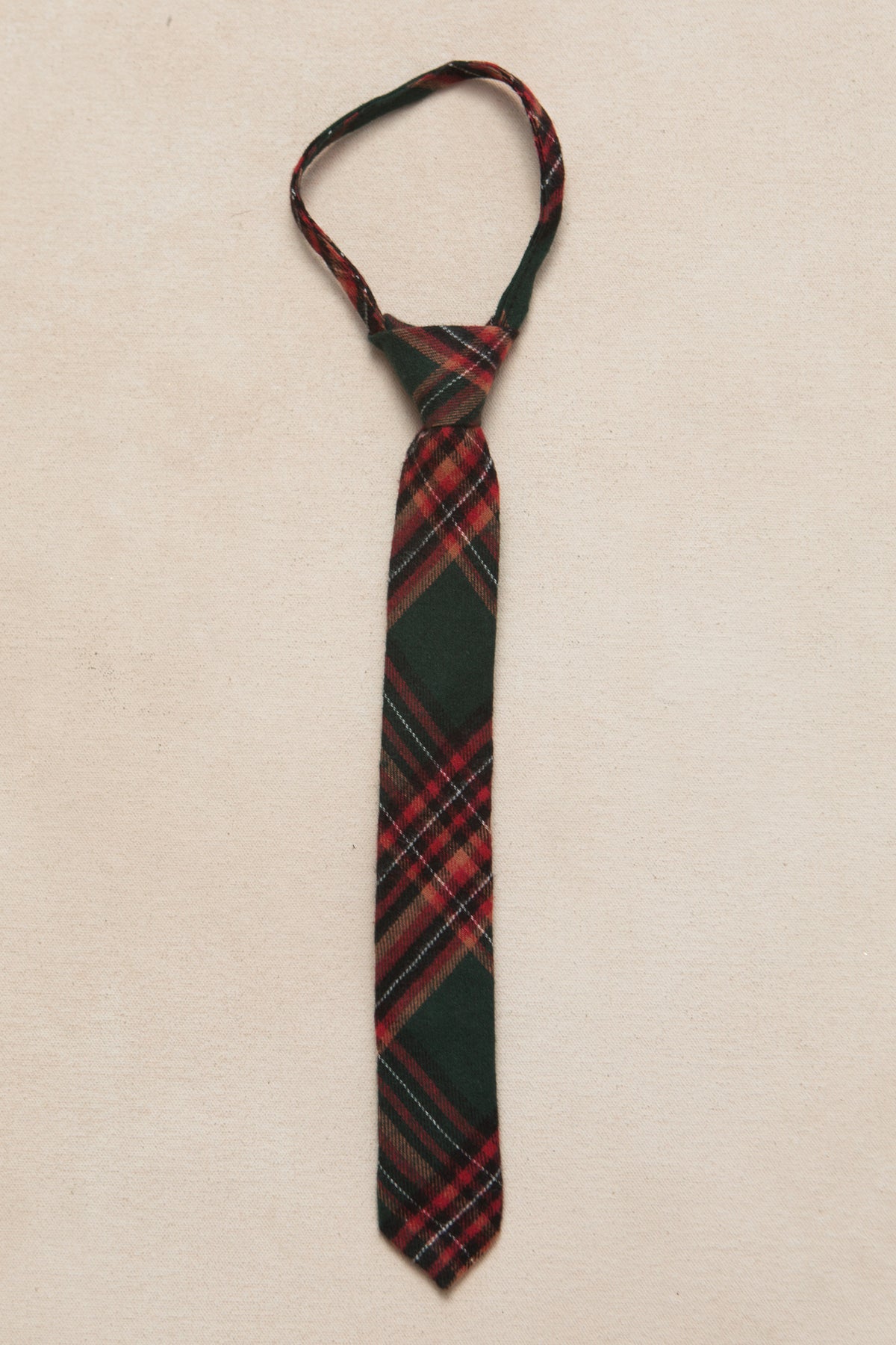 small boys green and red plaid tie on a cream background 