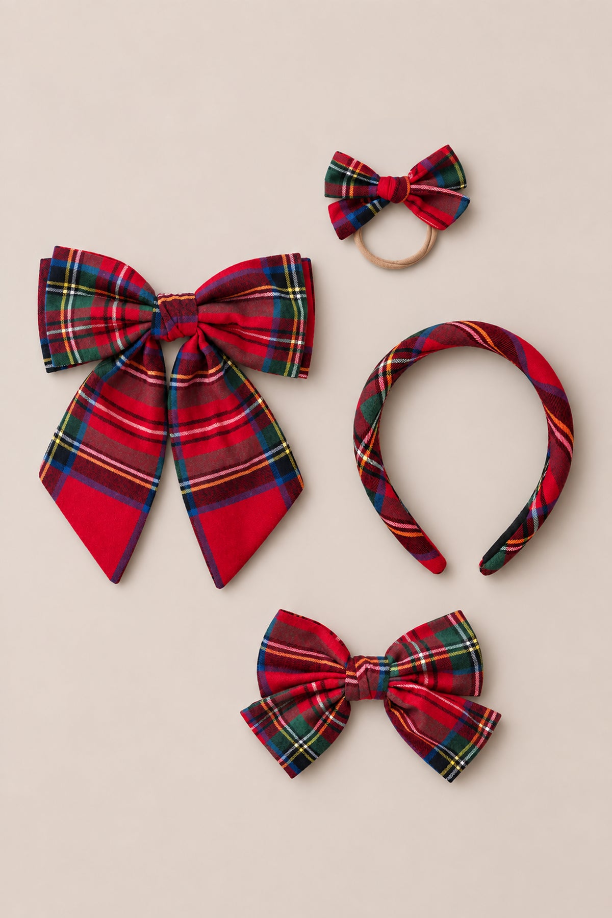 Four coordinating red cotton flannel hair accessories from Ivy City Co’s Hair Bows in Holiday Plaid collection—a large holiday bow, a plaid headband, a small-bow hair tie, and a medium bow—artfully arranged on a neutral background.