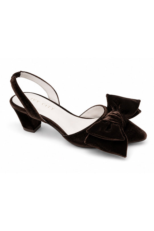 The Eloise Bow Heel in Brown by Ivy City Co is a brown velvet slingback shoe with a mid-height block heel and a large decorative bow on the front, featuring a comfortable leather insole, shown against a white background.
