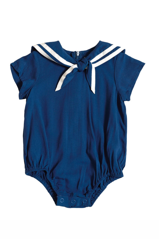 The Ivy City Co Baby Sailor Romper in Navy is a short-sleeve romper with a classic sailor collar, white stripes and a front tie, elastic leg openings, and convenient snap buttons at the bottom—making it the perfect charming nautical outfit for your little one.