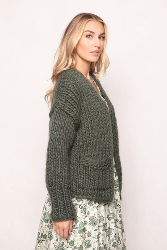 Woman wearing a green chunky knit sweater against a white background