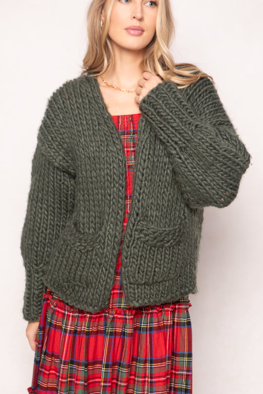 model wearing a green chunky cardigan over a red plaid dress on a white background 