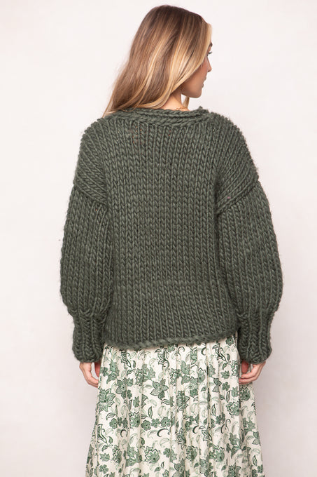 Person wearing a green knitted sweater and floral skirt on a plain background