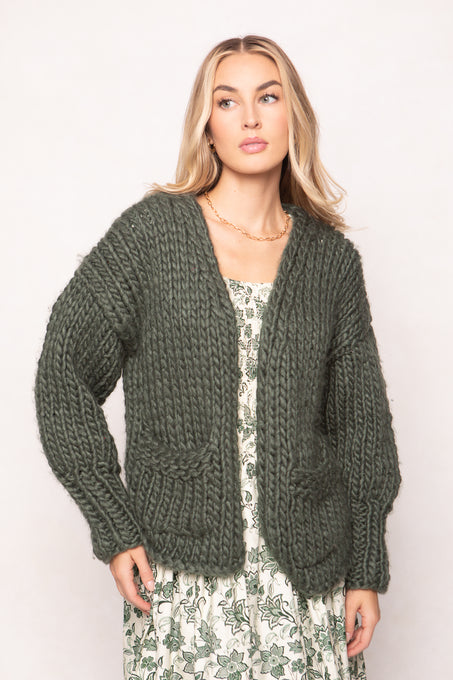 Woman wearing a green chunky knit cardigan against a plain background