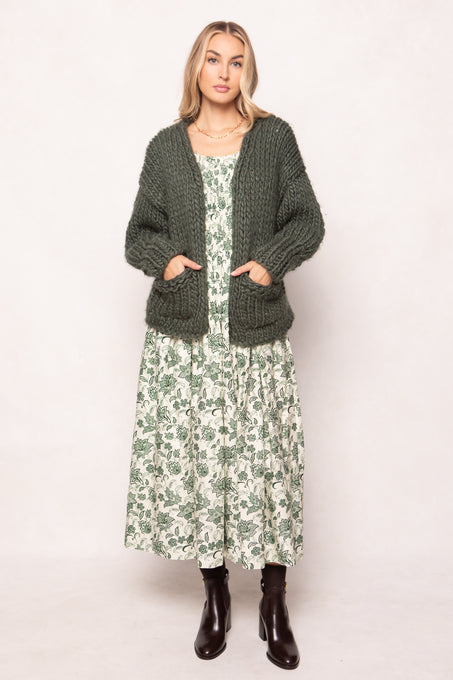 Woman wearing a green cardigan over a floral dress on a white background