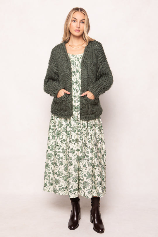 Woman wearing a green cardigan over a floral dress on a white background