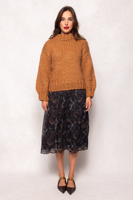 Woman wearing a mustard yellow sweater and black patterned skirt on a white background
