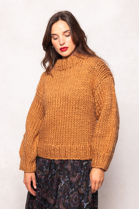 Woman wearing a mustard yellow knitted sweater against a white background