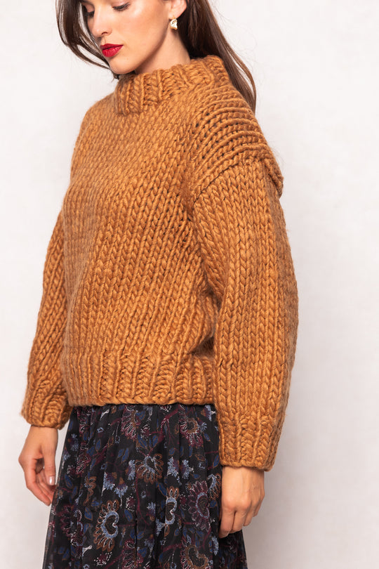Woman wearing a brown chunky knit sweater against a white background