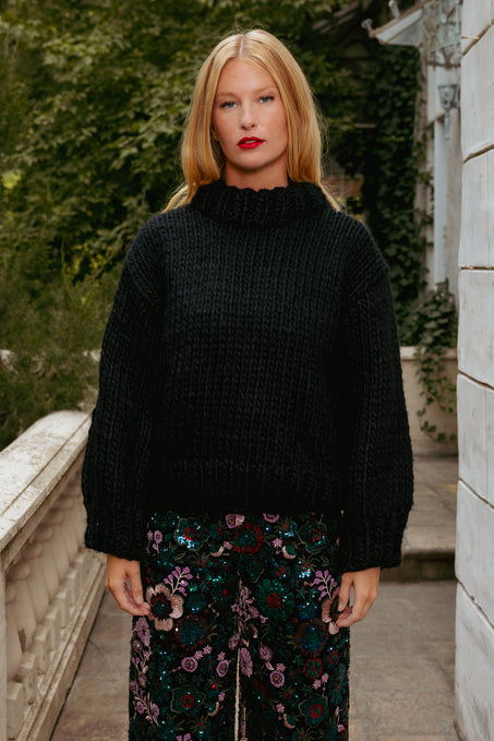 Woman wearing a black sweater and floral skirt standing outdoors.
