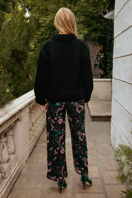 Person wearing a black jacket and floral pants walking on a stone path.