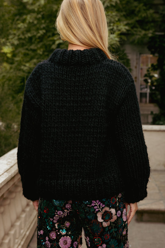 Person wearing a black knitted sweater with floral pants outdoors