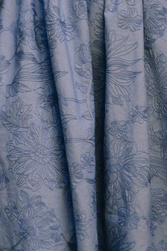 Close-up of the Isla Dress in Floral Embroidered Chambray by Ivy City Co, showcasing embossed flowers and leaves in blue thread on pleated fabric, emphasizing the dress’s intricate, delicate details.