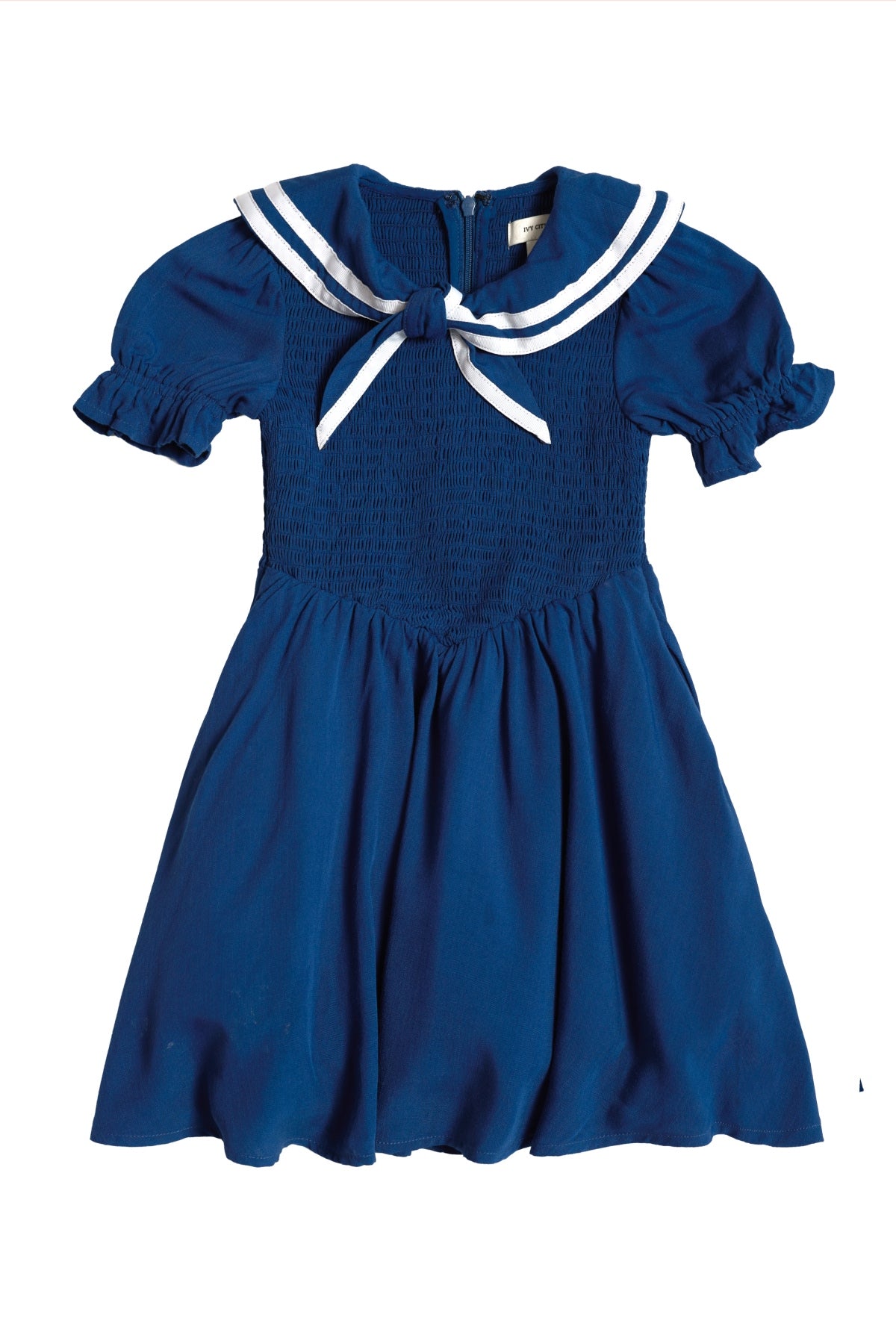 The Mini Alice Dress in Navy by Ivy City Co is a charming blue smocked dress featuring puffed sleeves, a smocked bodice, and a white sailor-style collar with coordinating bow and trim. Perfect for creating adorable Mom and Me matching moments, it is pictured laid flat on a white background.