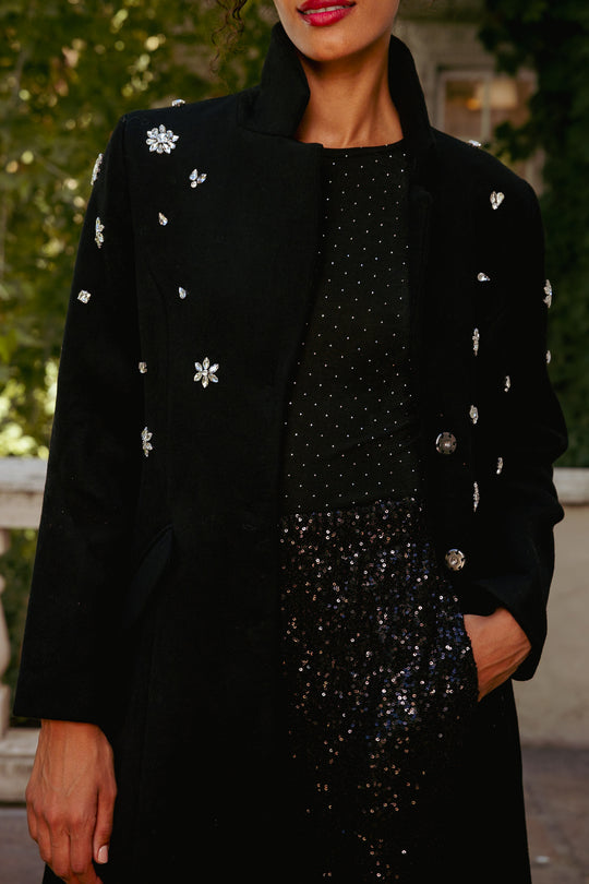 Person wearing a black coat with floral embellishments and a black sequin dress.