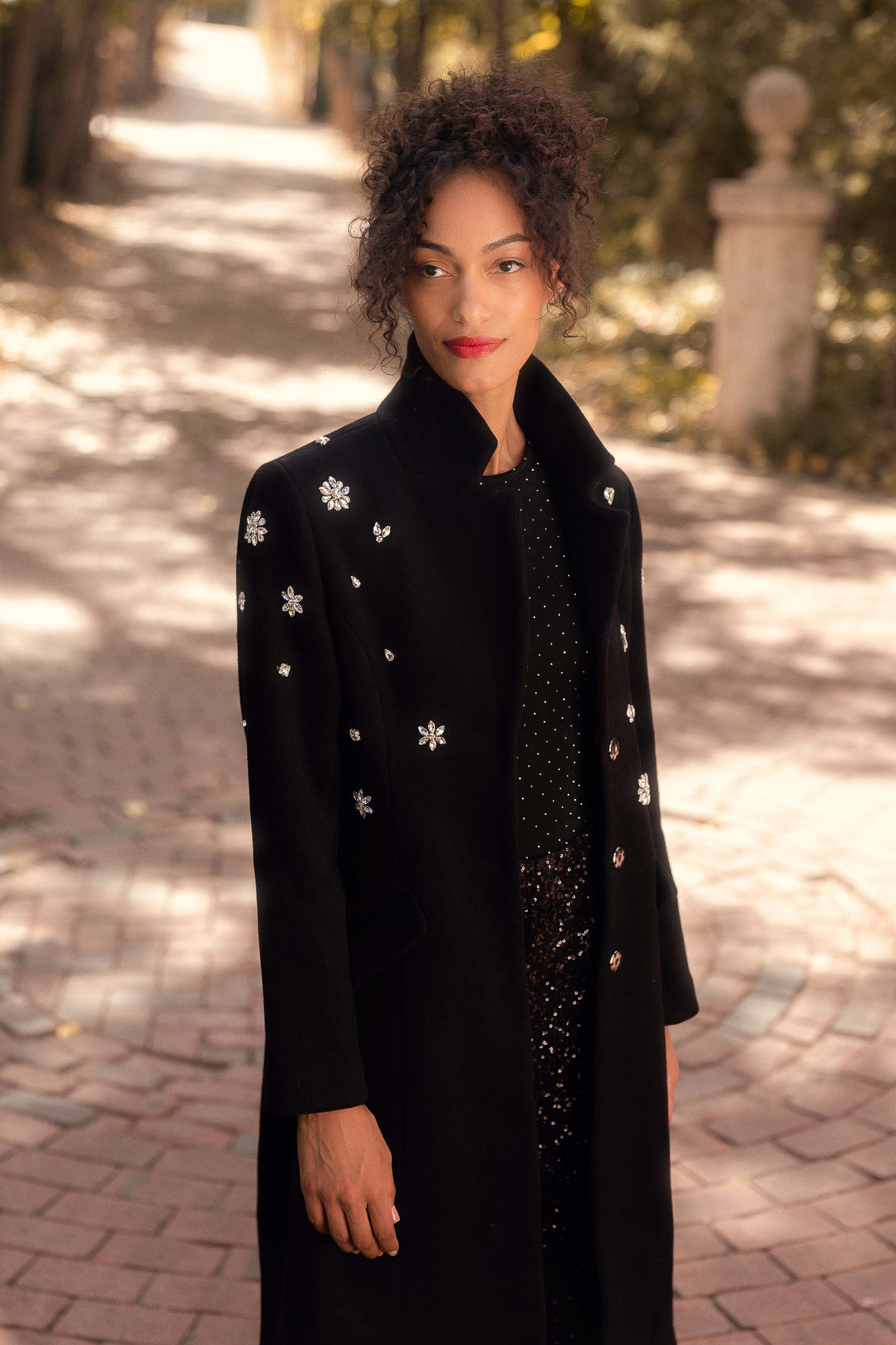 Woman wearing a black coat with white floral patterns on a paved path.