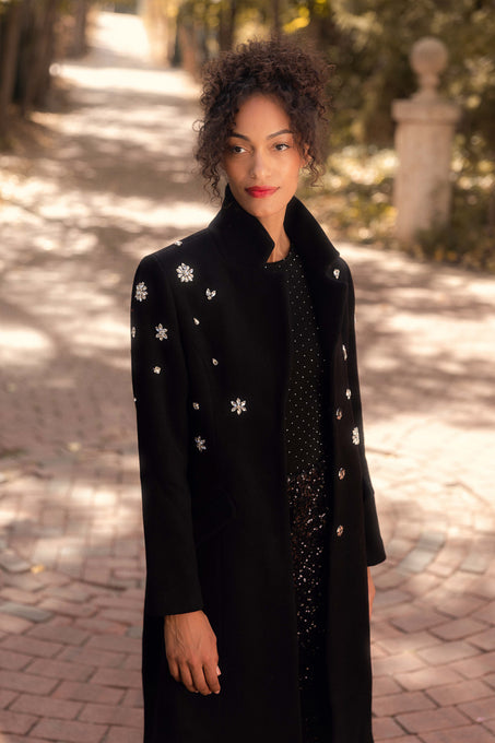 Woman wearing a black coat with white floral patterns on a paved path.