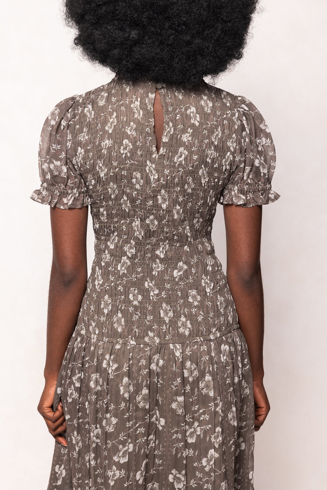 Person wearing a floral dress with short sleeves against a white background