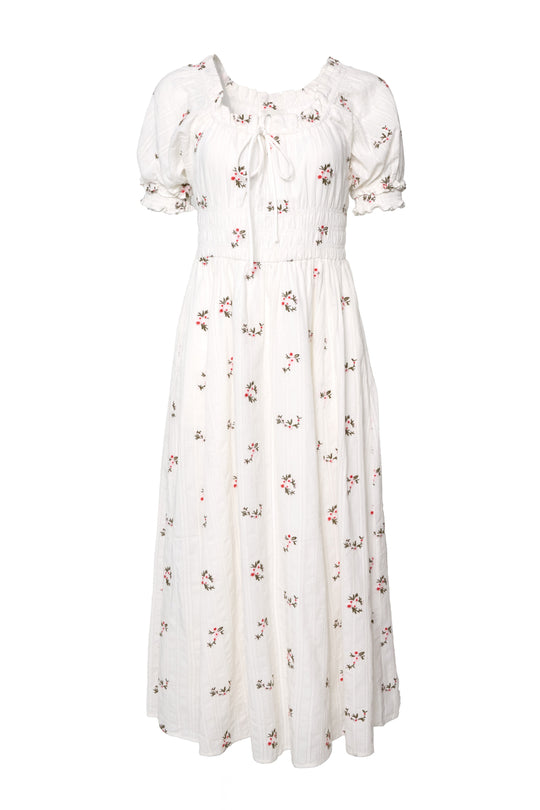 The Jessie Dress in Ditsy Embroidery by Ivy City Co is a white, ankle-length cotton dress featuring short sleeves, a smocked bodice, ruffled neckline, and scattered small floral embroidery.