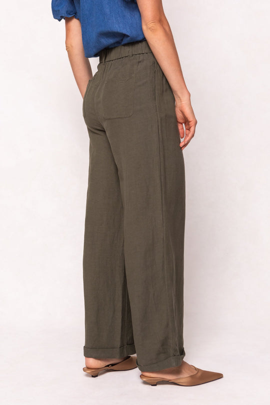 A person wearing olive green, linen-blend Veronica Pants in Green featuring a high-waisted, wide-leg fit with an elastic waistband and cuffed hems.