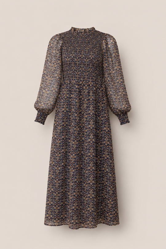 The Jordan Dress in Midnight Moroccan Tile by Ivy City Co is an ankle-length maxi dress featuring long balloon sleeves, a high ruffled neckline, and a striking blue and tan floral paisley pattern on sheer fabric—an elegant choice for evening wear or making a statement at any special occasion.