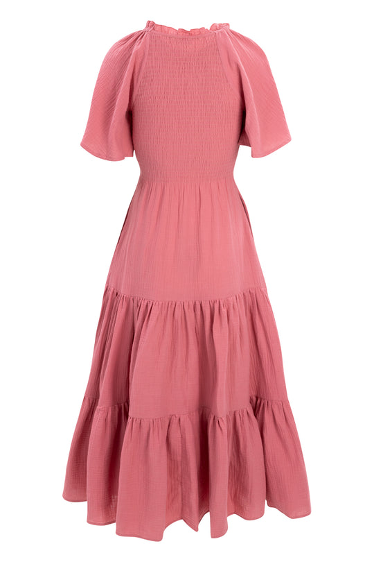 The Ivy City Co Jovie Dress in Pink features short sleeves, cotton gauze fabric, a ruffled neckline, smocked bodice, and tiered flowy skirt—shown from the back and designed to be a comfortable maternity-friendly option.