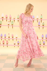 Woman in a pink floral dress standing in front of an ice cream cone display.