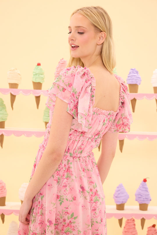 Woman in a pink floral dress standing in front of ice cream cone decorations on a yellow background