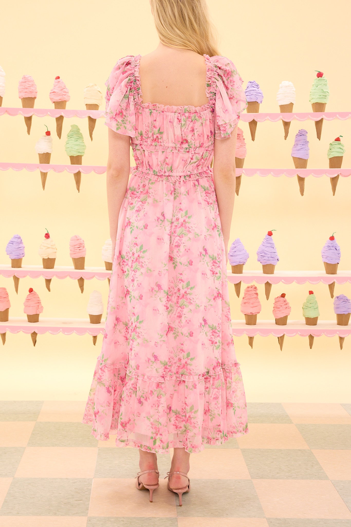 Woman wearing a pink floral dress standing in front of an ice cream cone pattern.