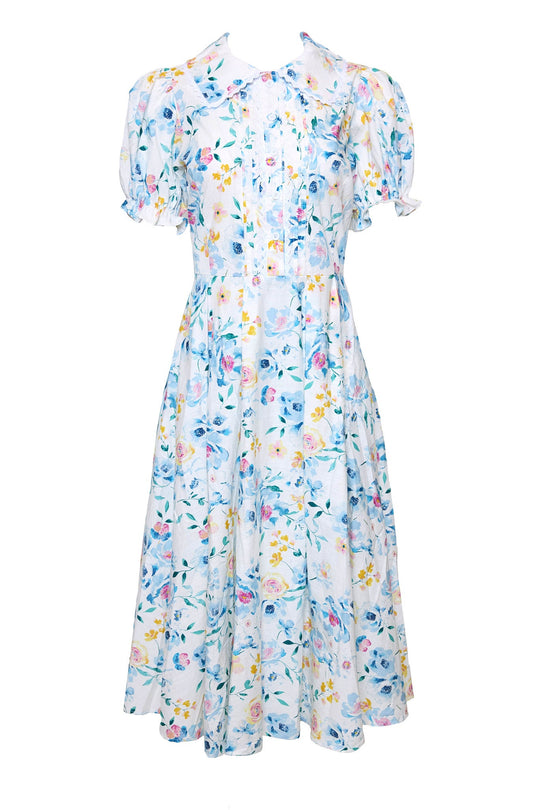 The Sophia Dress in Blue Bouquet by Ivy City Co is a white, short-sleeved midi dress adorned with a pastel blue, yellow, and pink floral pattern. This nursing-friendly dress features buttons down the front and a slightly flared skirt.