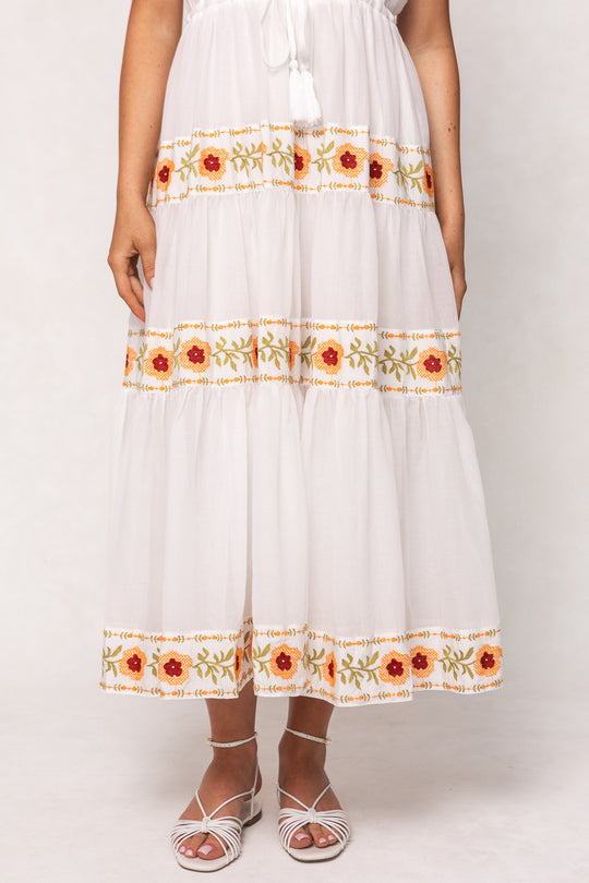 A person wearing the Ivy City Co Katerina Dress in White with Floral Trim and white strappy sandals stands against a neutral background.