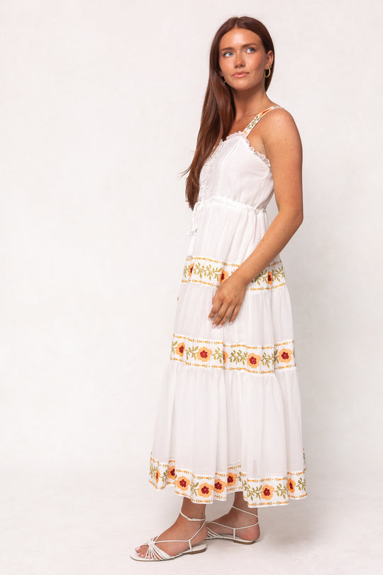 A woman with long auburn hair wears the Ivy City Co Katerina Dress in White with Floral Trim and white strappy sandals, standing against a plain light background.