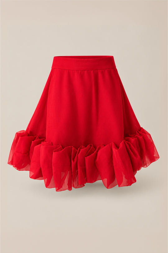 The Kendy Skirt in Poinsettia by Ivy City Co features a vibrant red hue, a flared silhouette, and a ruffled hem, all crafted from sheer organza. Displayed on a plain light background, this elegant skirt is the perfect choice for your next holiday party.