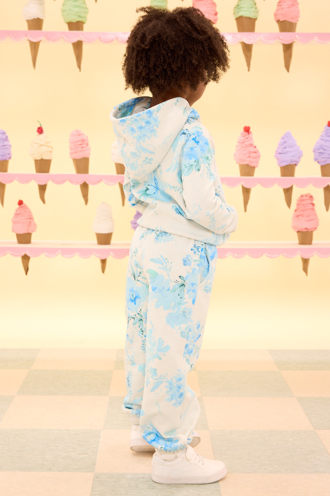the back of a child wearing a blue floral hoodie against a yellow ice cream cone wall