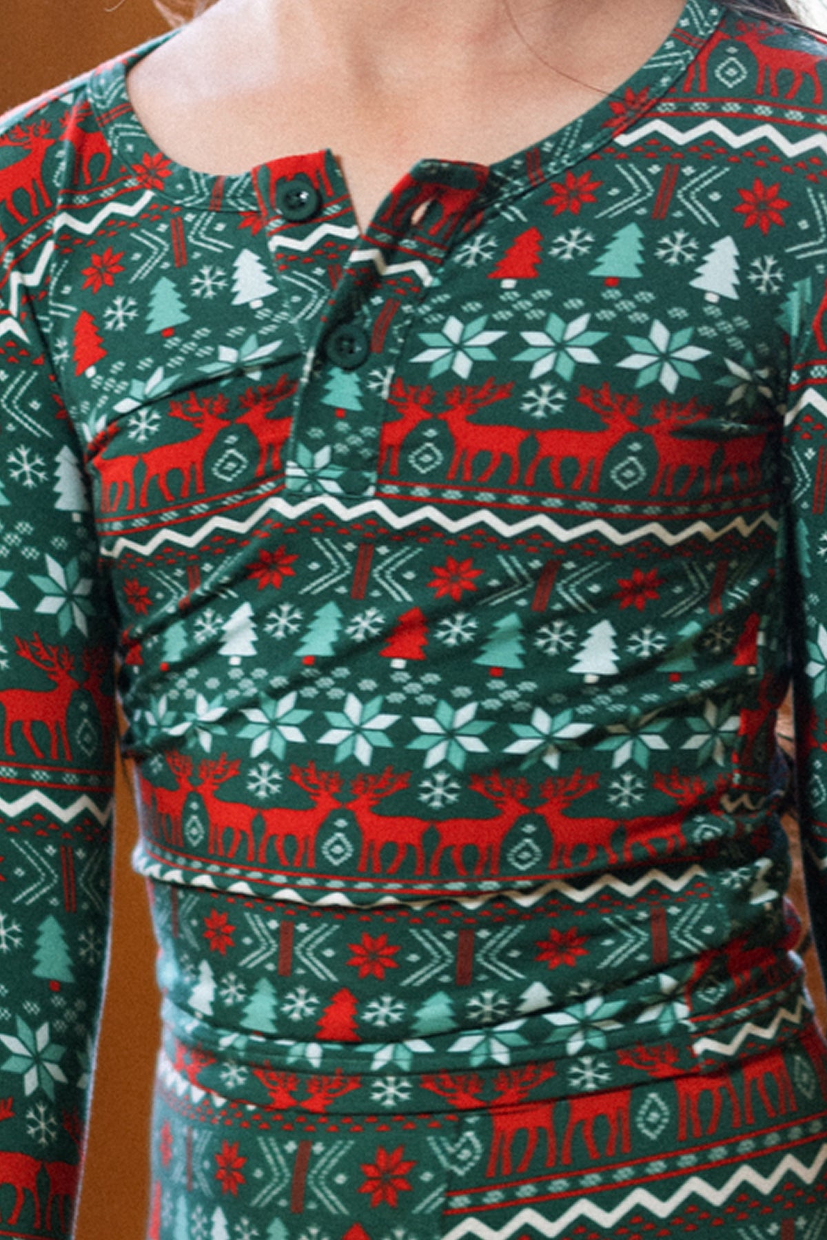 A child wears the Kids So Soft Pajama Set in Alpine Noel by Ivy City Co—green pajamas with festive red, white, and light blue holiday patterns and a collared, buttoned pajama top—perfect for family matching.