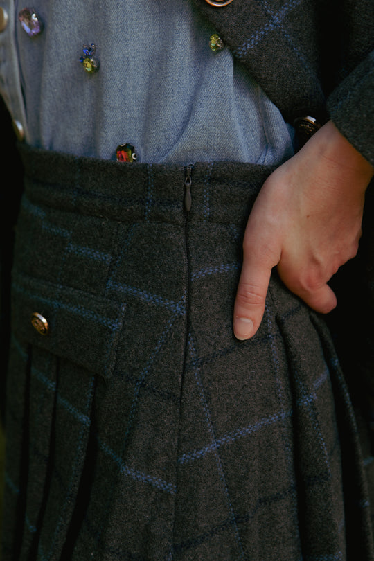 A close-up of a hand in the pocket of the Kinley Skirt in Charcoal Plaid by Ivy City Co, paired with a blue embellished shirt and matching plaid jacket.