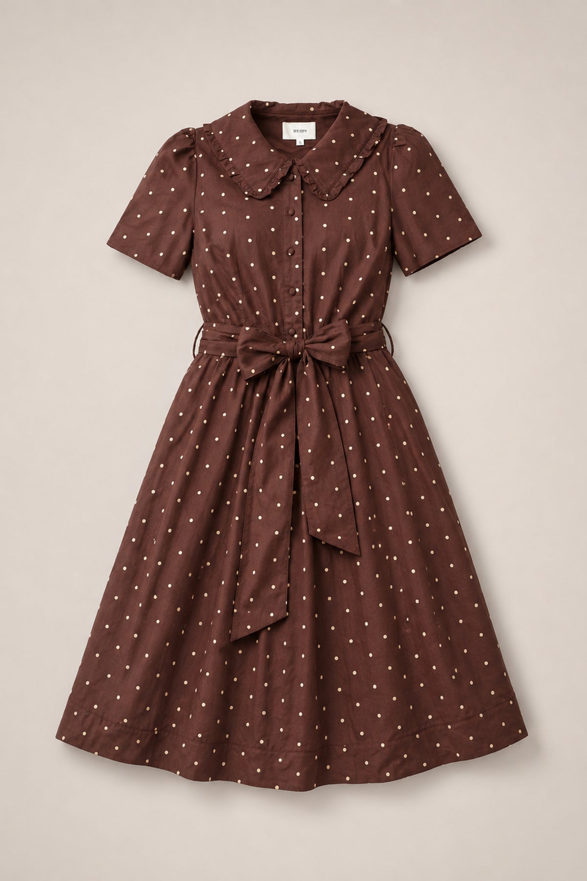 The Kit Dress in Warm Cocoa Dainty Dot by Ivy City Co is a brown, knee-length cotton midi dress featuring white polka dots, short sleeves, a Peter Pan collar, a nursing-friendly button-down front, and a matching fabric belt that ties at the waist—capturing timeless charm in every detail.